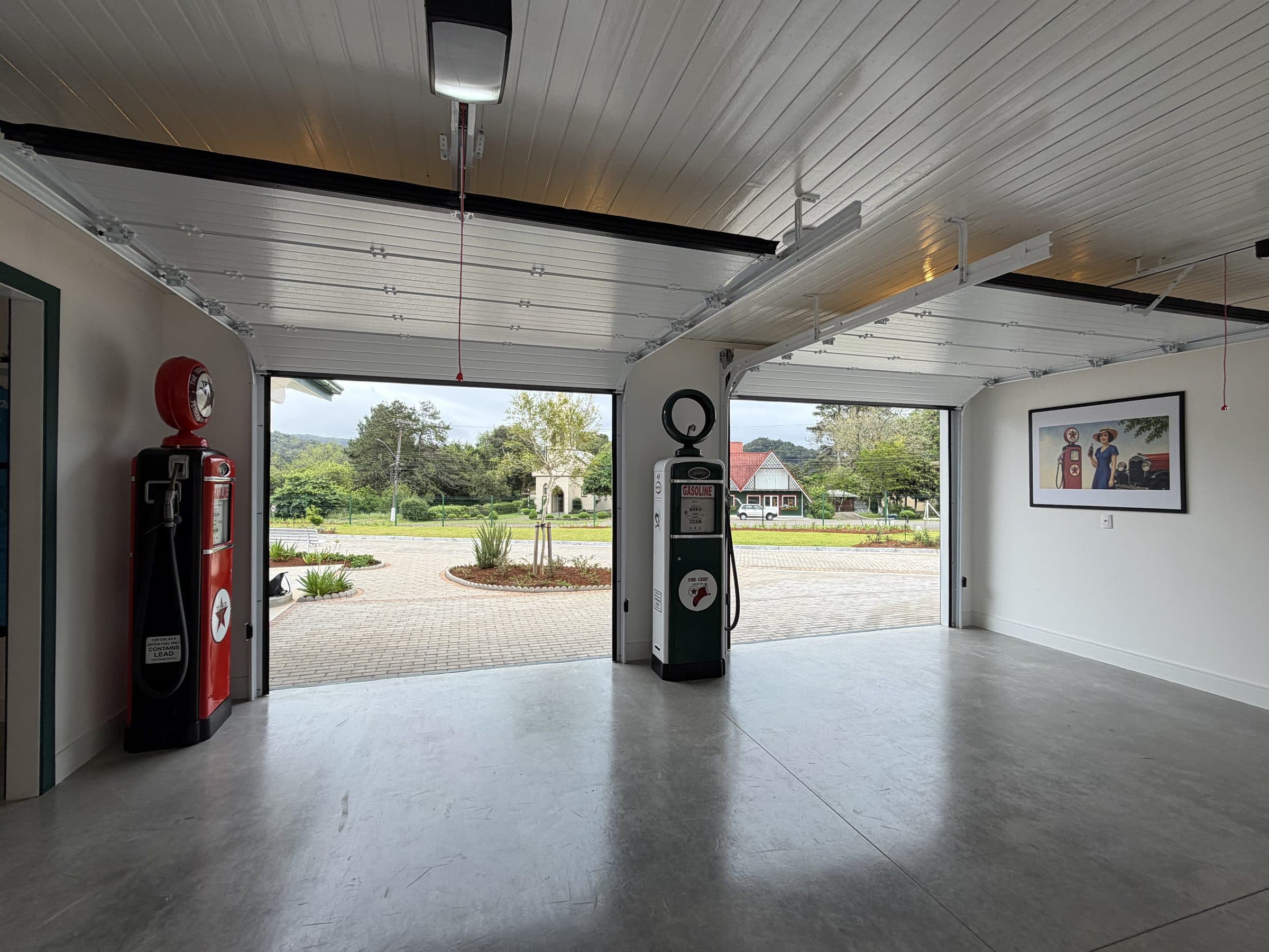 Obra Cattani: garagem com dois portões seccionais abertos, painéis guardados no teto e bombas de gasolina antigas